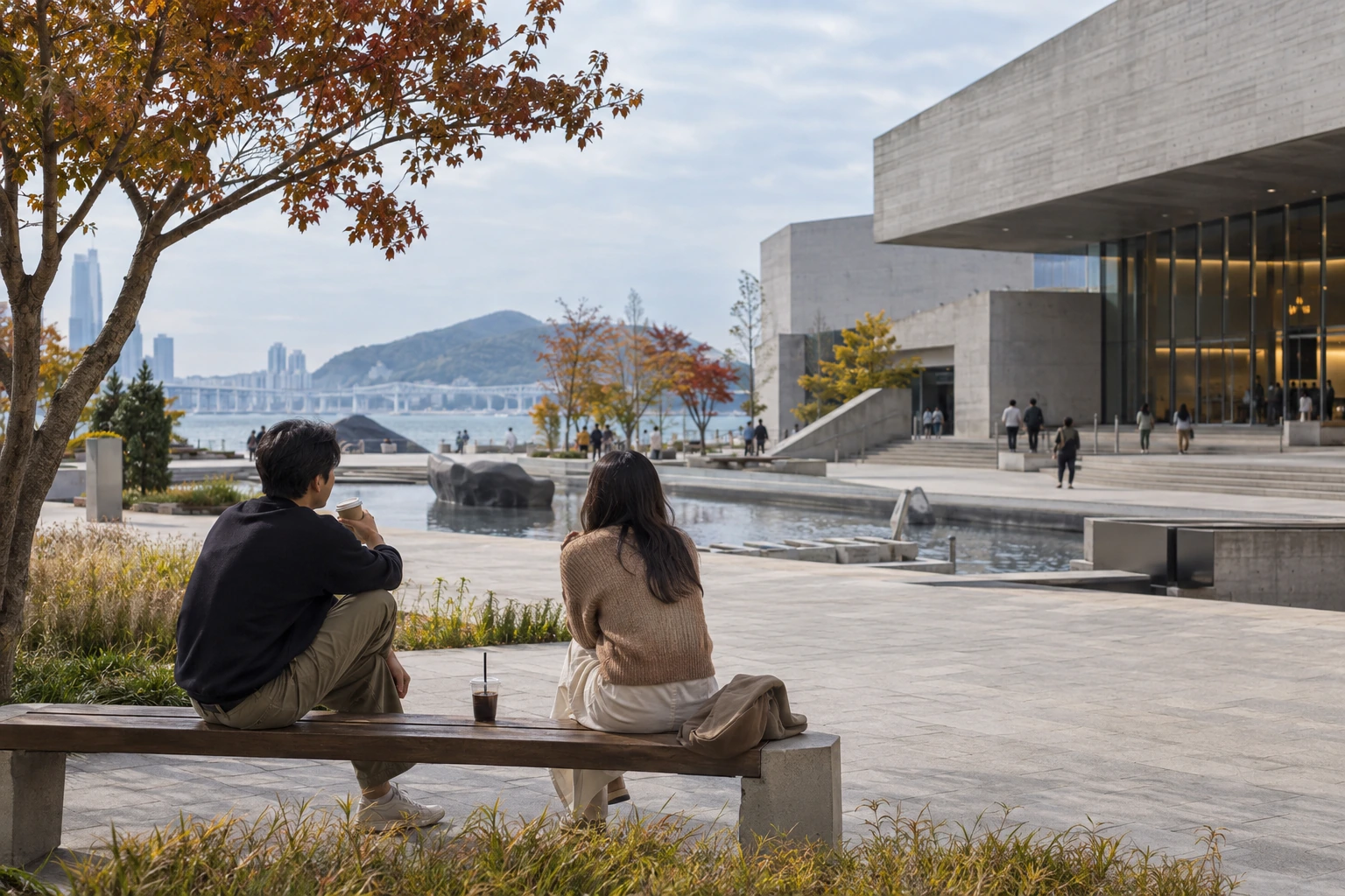 Two adults resting with cafe drinks on a bench outside a modest contemporary cinema building on an overcast autumn afternoon.