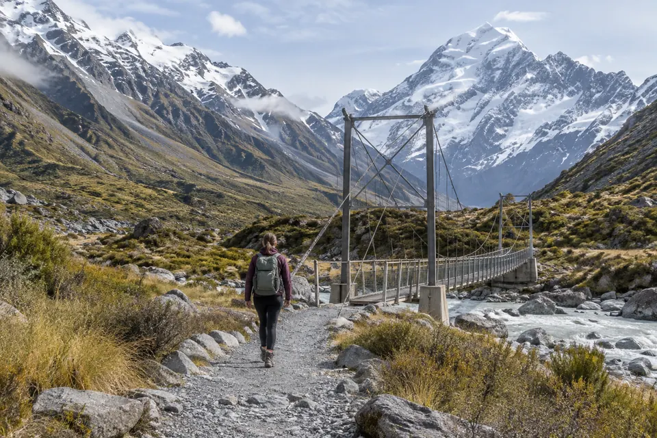 AI illustration of one walker approaching a generic alpine suspension bridge in a mountain valley.