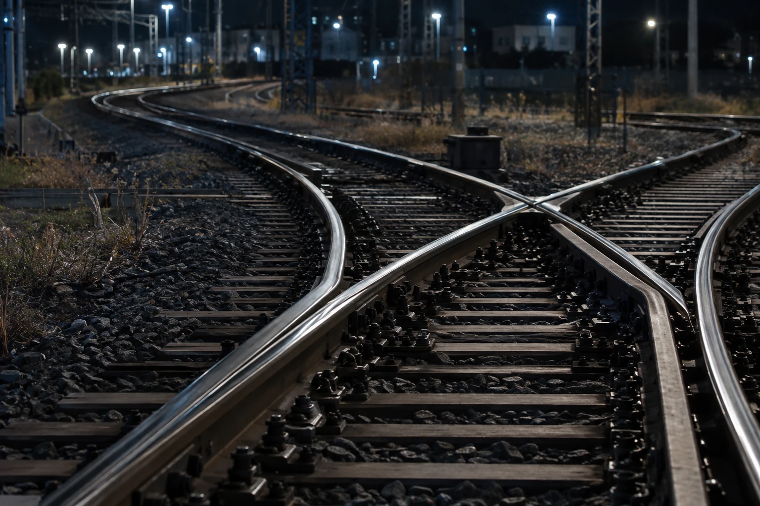 Close view of railway switch rails under cool night lighting, illustrating route changes.